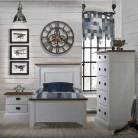 White Bedroom with wood panelled walls, blue curtain and sheets with white wooden twin bed, two drawer nightstand, and 5 drawer dresser with black metallic handles