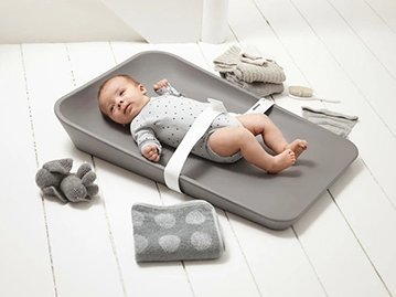Baby laying on grey changing mat on the floor with safety belt attached